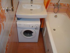 Máquina de lavar roupa debaixo da pia no banheiro